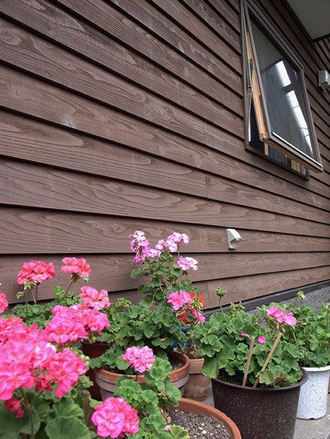 塗り壁と下見板によく似合うスウェーデン製の木製サッシ。庭に咲く草花が引き立つ外観が目を引く